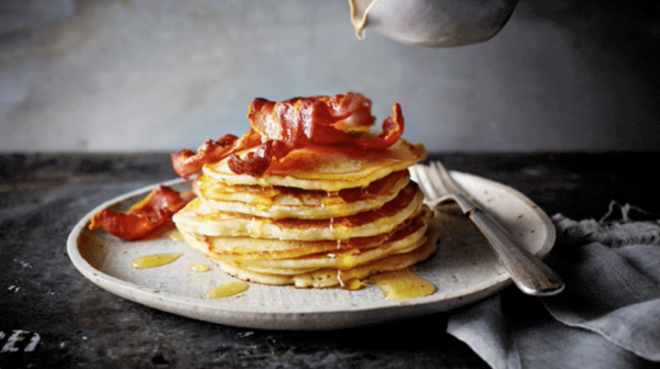 Food videography showing a stack of American pancakes, topped with bacon and being topped with syrup