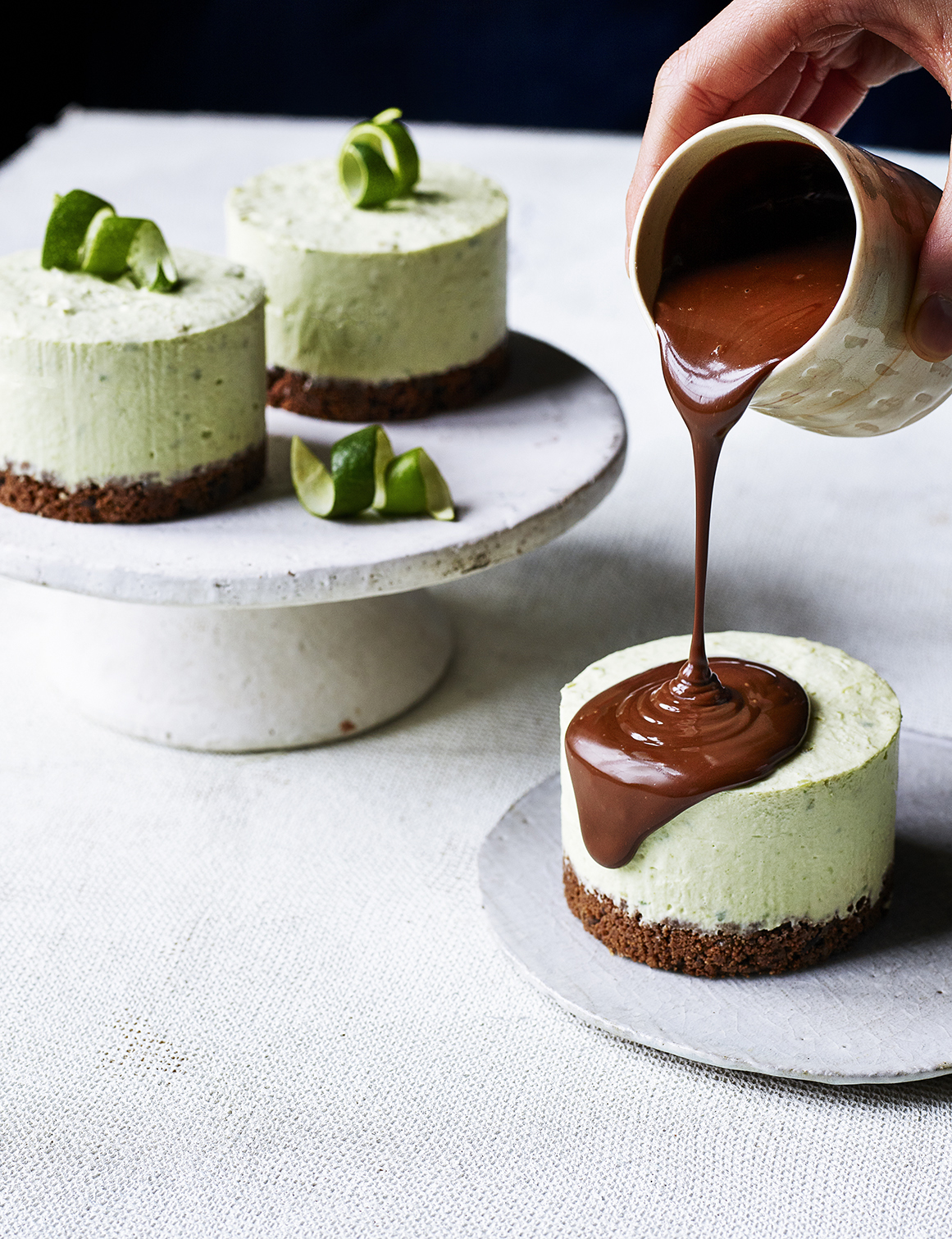 Food photography showing two cheesecakes, topped with avocado and a third having melted chocolate poured over