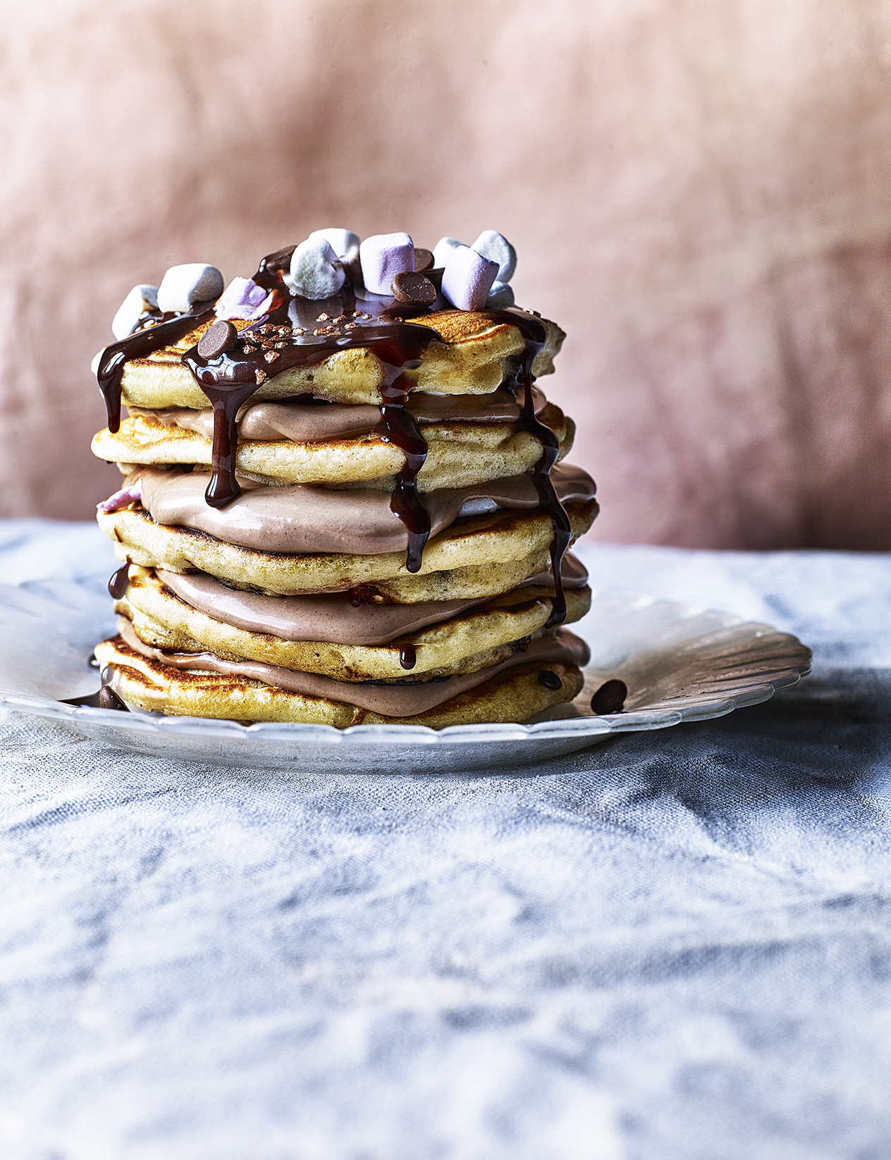 Food photography showing a stack of pancakes, topped with chocolate sauce and mini marshmallows