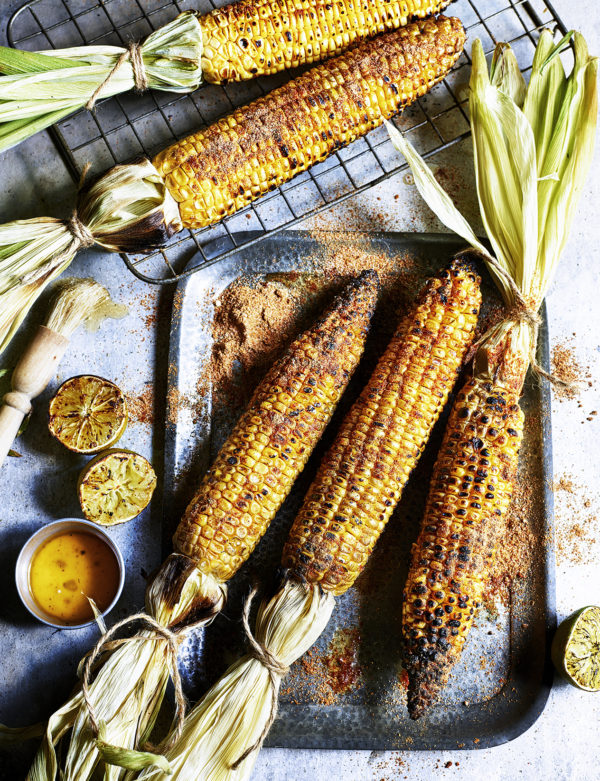 Food photography showing whole griddled sweetcorn, with limes and melted butte