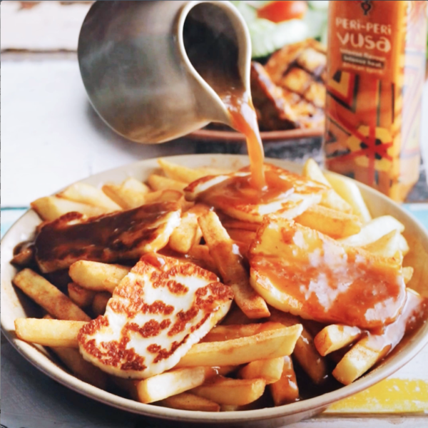 Food videography showing a plate of chips, topped with halloumi cheese, with a sauce being poured over