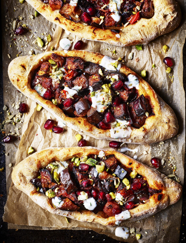 Food product photography showing pide bread displayed on a wooden platter, topped with aubergine and feta cheese