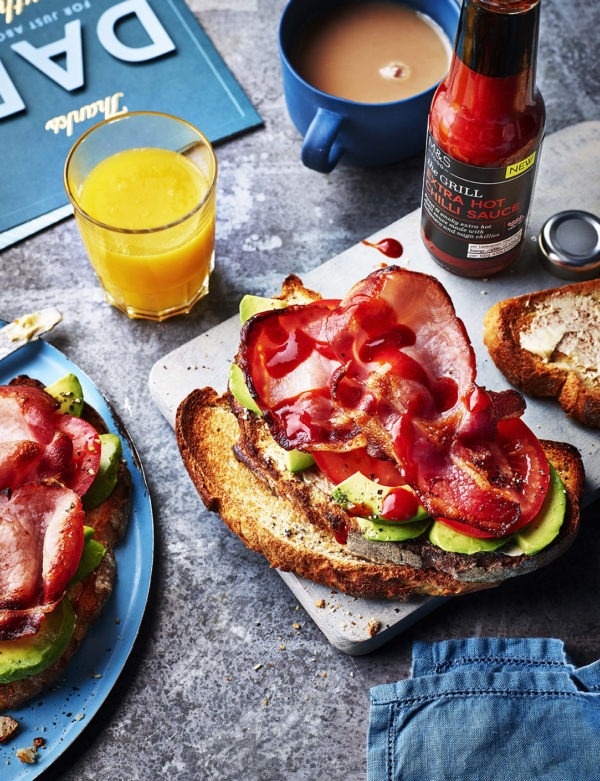 Food photography for advertising showing bacon and avocado on brown bread with a class of orange juice and cup of tea.